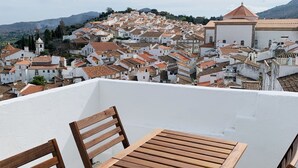 A wooden table and chairs on a rooftop terrace overlooking a town with terracotta-roofed buildings and a hill in the background. - House by the Castle (360 panoramic View) (Castelo de Vide)