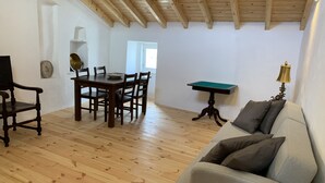 A room with a wooden floor, a dining table with chairs, a sofa, a small table with a lamp, and a wall-mounted shelf. - House by the Castle (360 panoramic View) (Castelo de Vide)