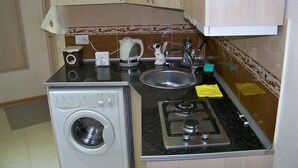 Une cuisine compacte équipée d’un lave-linge, d’une cuisinière, d’un évier et de divers ustensiles de cuisine.