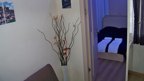 Une pièce comprenant un lit, une table de chevet, un vase avec des branches et un tableau accroché au mur.