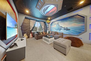 A room with a large TV, a sofa, a coffee table, and a painting of a spaceship. - Encore Villa with Magical Kids' Rooms & Theater (Kissimmee)