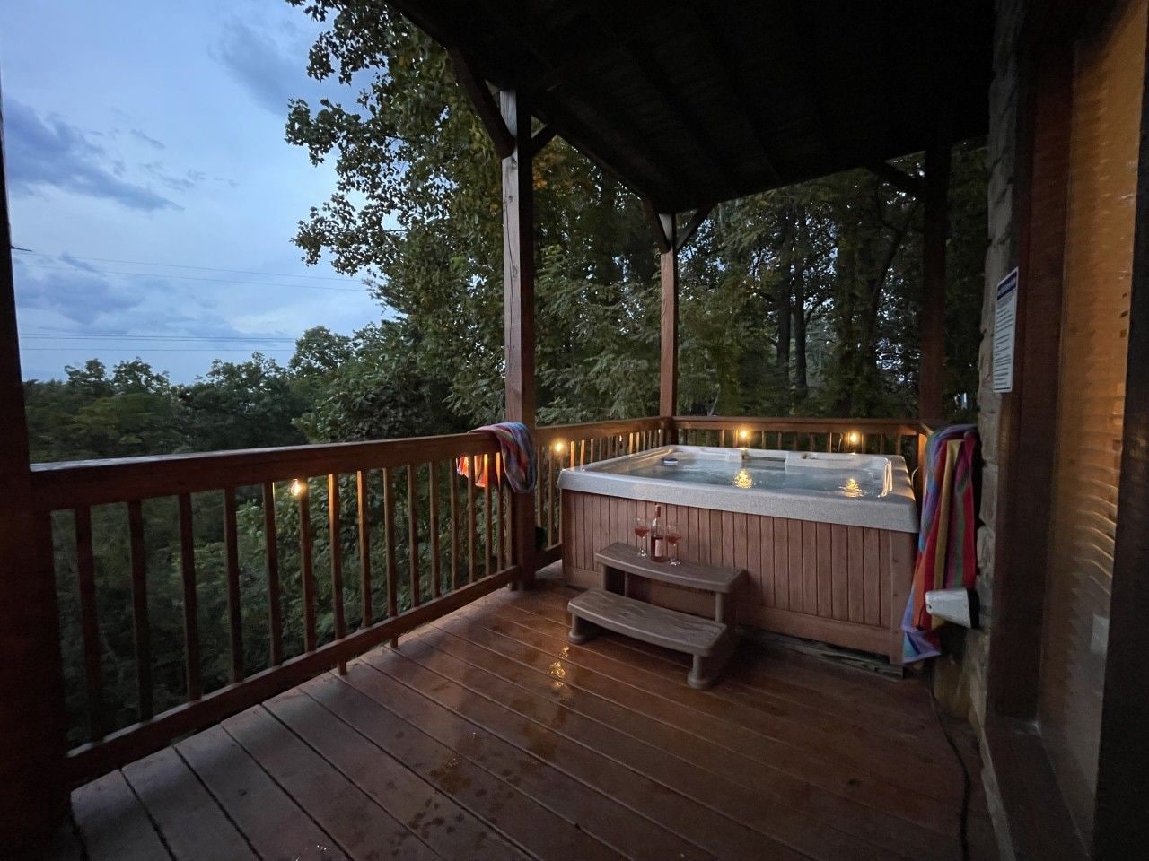A wooden deck with a hot tub and a bench, surrounded by trees.