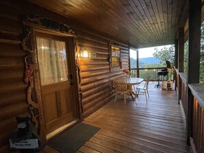 A wooden cabin with a porch, a dining table, and chairs.