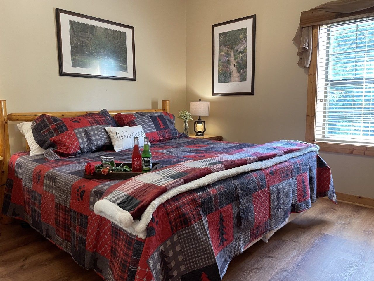 A bed with a red and black quilt, a bedside table with a lamp, and two framed pictures on the wall.