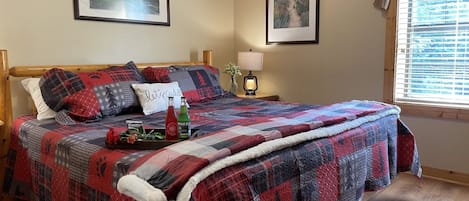 A bed with a red and black quilt, a bedside table with a lamp, and two framed pictures on the wall.