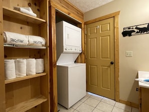 A laundry area with a washer and dryer, wooden shelves with towels, and a door with a bear silhouette decoration. - Honey Bear | 2 King Suites, FirePit, HotTub, Views, Pets (Sevierville)