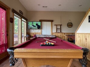 Una mesa de billar con bolas, un televisor y paredes de madera.