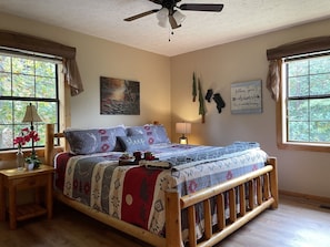 A cozy bedroom with a wooden bed frame, a ceiling fan, and a large window with curtains.