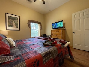 A bedroom with a bed, a television, a dresser, a door, and a window with curtains. - Honey Bear | 2 King Suites, FirePit, HotTub, Views, Pets (Sevierville)