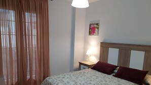 Une chambre à coucher avec un lit, une table de chevet, une lampe et une fenêtre avec des rideaux.