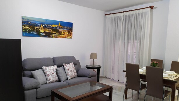 Un salon comprenant un canapé, une table basse, une table à manger avec des chaises, une lampe et un tableau représentant un paysage urbain.