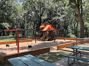 Explore the park's playground with a swing set, climbing structure, and sandpit, surrounded by lush trees.