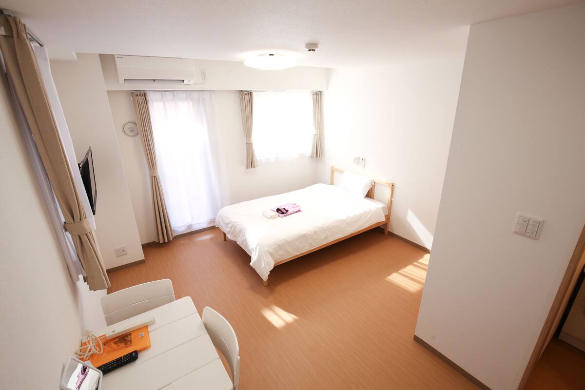 Habitación de hotel con una cama individual, un escritorio con silla, un televisor de pantalla plana y una ventana con cortinas.