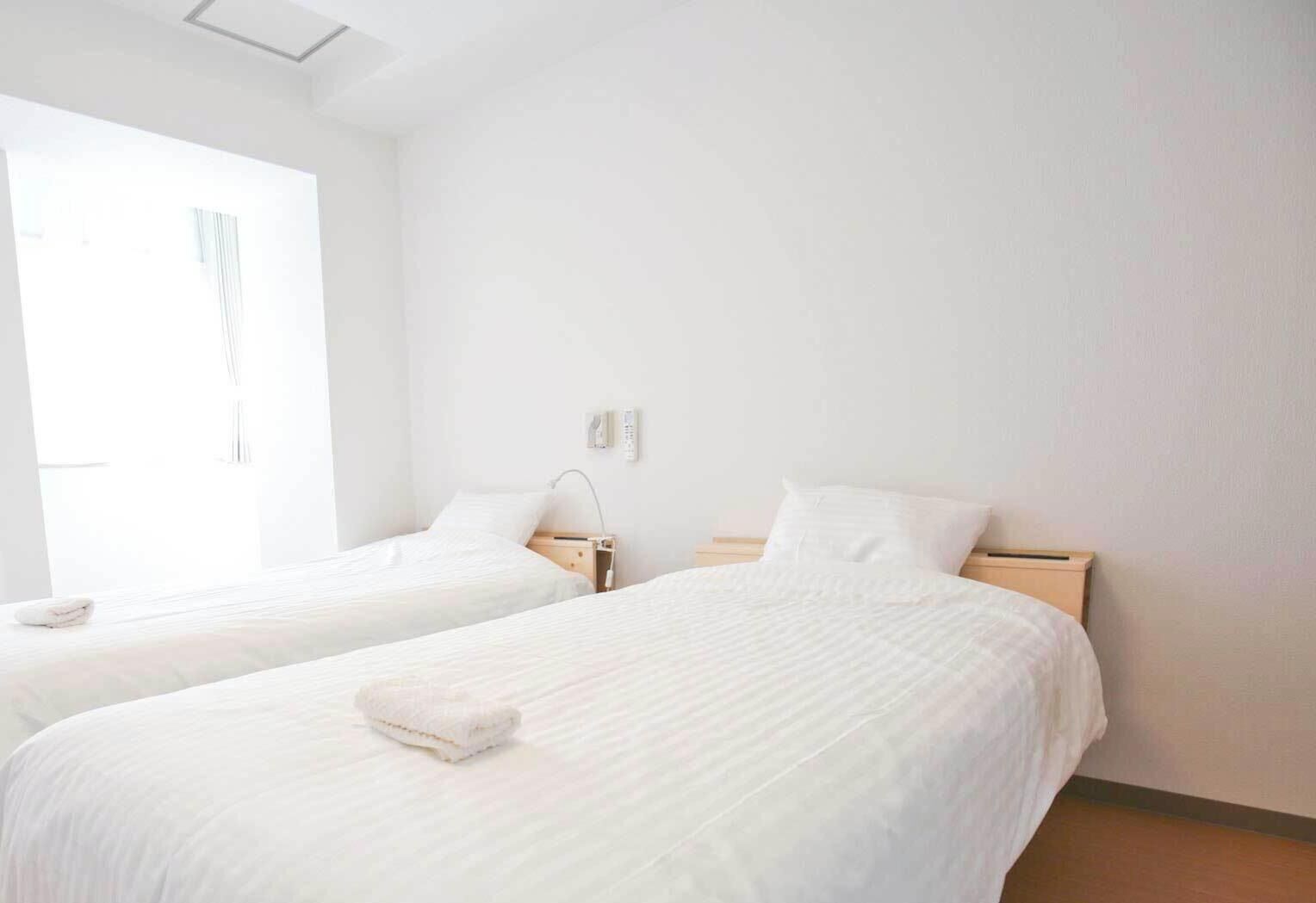 Hotellihuone, jossa on kaksi sänkyä, yöpöytä, lamppu ja ikkuna.