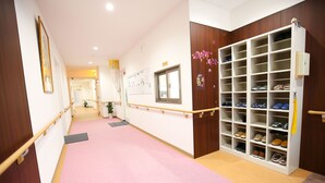 A hallway with a pink carpet, wooden walls, a white shoe rack, and a wooden railing.