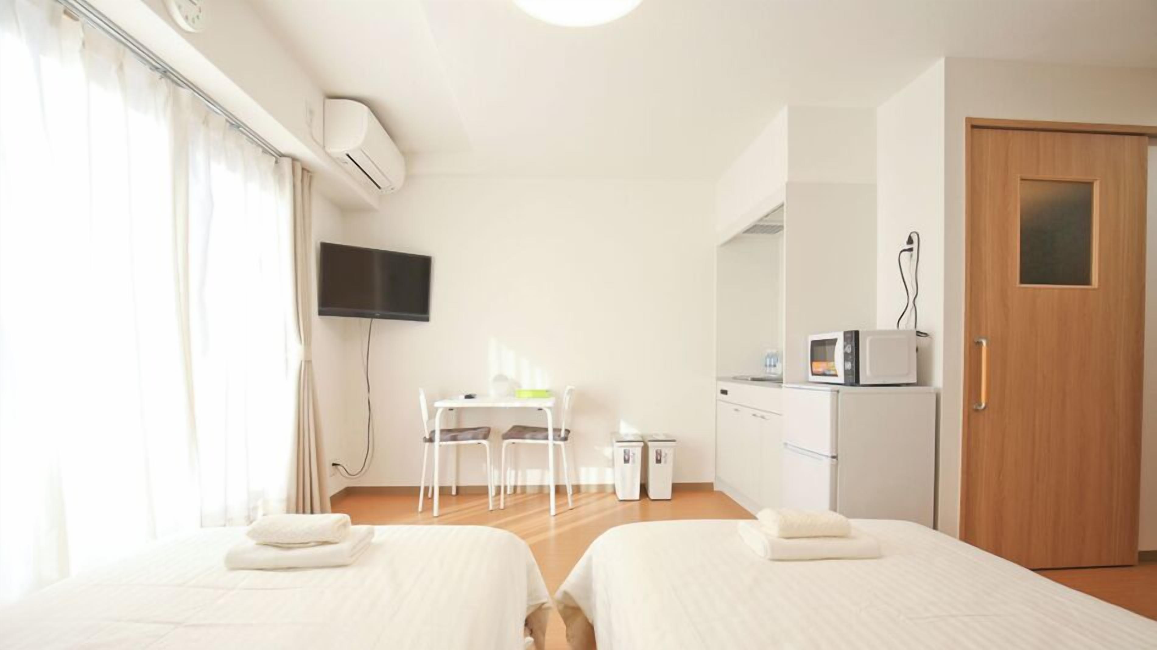 Une chambre d’hôtel avec deux lits, un bureau, une télévision, un four à micro-ondes et une porte.