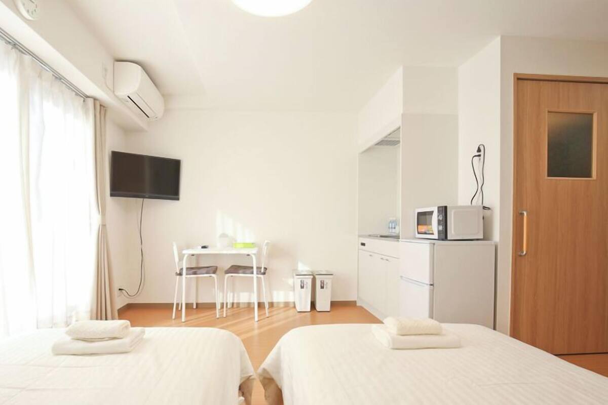 Habitación de hotel con dos camas, un escritorio, un televisor, un microondas y una puerta.