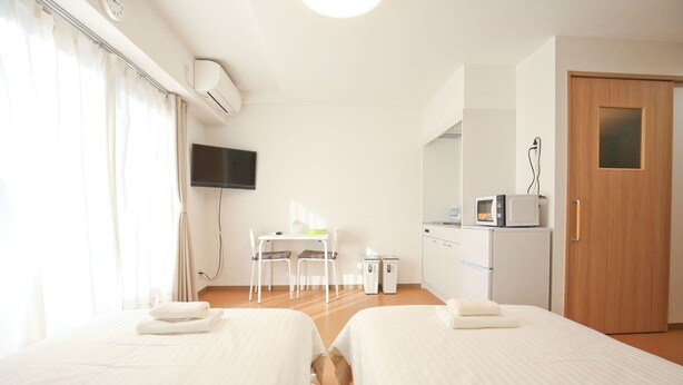 A hotel room with two beds, a desk with chairs, a television, a microwave, and a door.