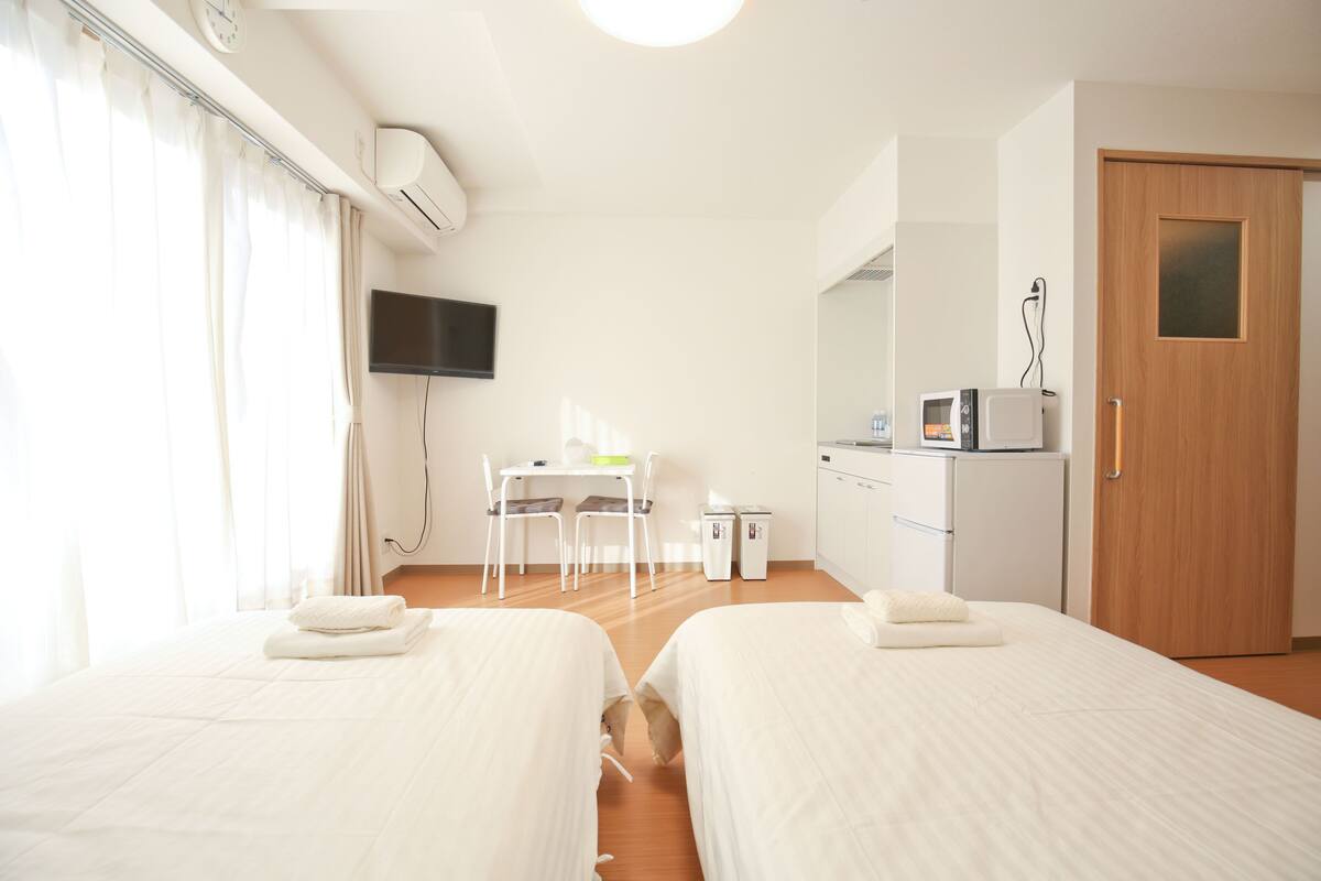 Habitación de hotel con dos camas, un escritorio con sillas, un televisor, un microondas y una puerta.