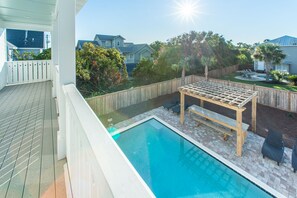 A backyard with a swimming pool, wooden deck, and outdoor furniture.