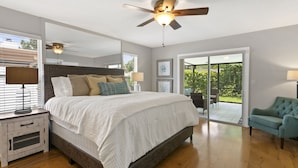 A bedroom with a large bed, a ceiling fan, and a sliding glass door leading to a patio. - Beautiful Coastal-style Oasis! Heated POOL. 5min to BEACH! 8 Guests. (Seminole)