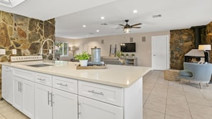 A spacious kitchen with a large island, white cabinetry, and a stone accent wall. - Beautiful Coastal-style Oasis! Heated POOL. 5min to BEACH! 8 Guests. (Seminole)