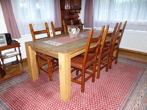 A dining area with a wooden table and six chairs, a radio on a side table, and a patterned rug. - Nice apartment for 6 people with WIFI, TV and balcony (Gerschnialp)