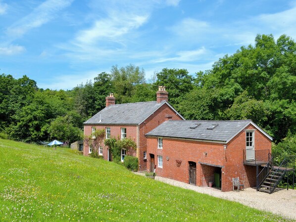 A red brick house with a sloped roof, a chimney, and a small porch with a bench.