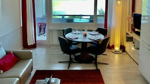 Ein Essbereich mit Tisch für vier Personen, einer Couch, einem Fernseher und Blick auf einen Pool im Freien.