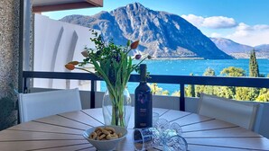 Ein Tisch mit Blumen in einer Vase, einer Weinflasche und einer Schüssel mit Snacks auf einem Balkon mit Blick auf die Berge.