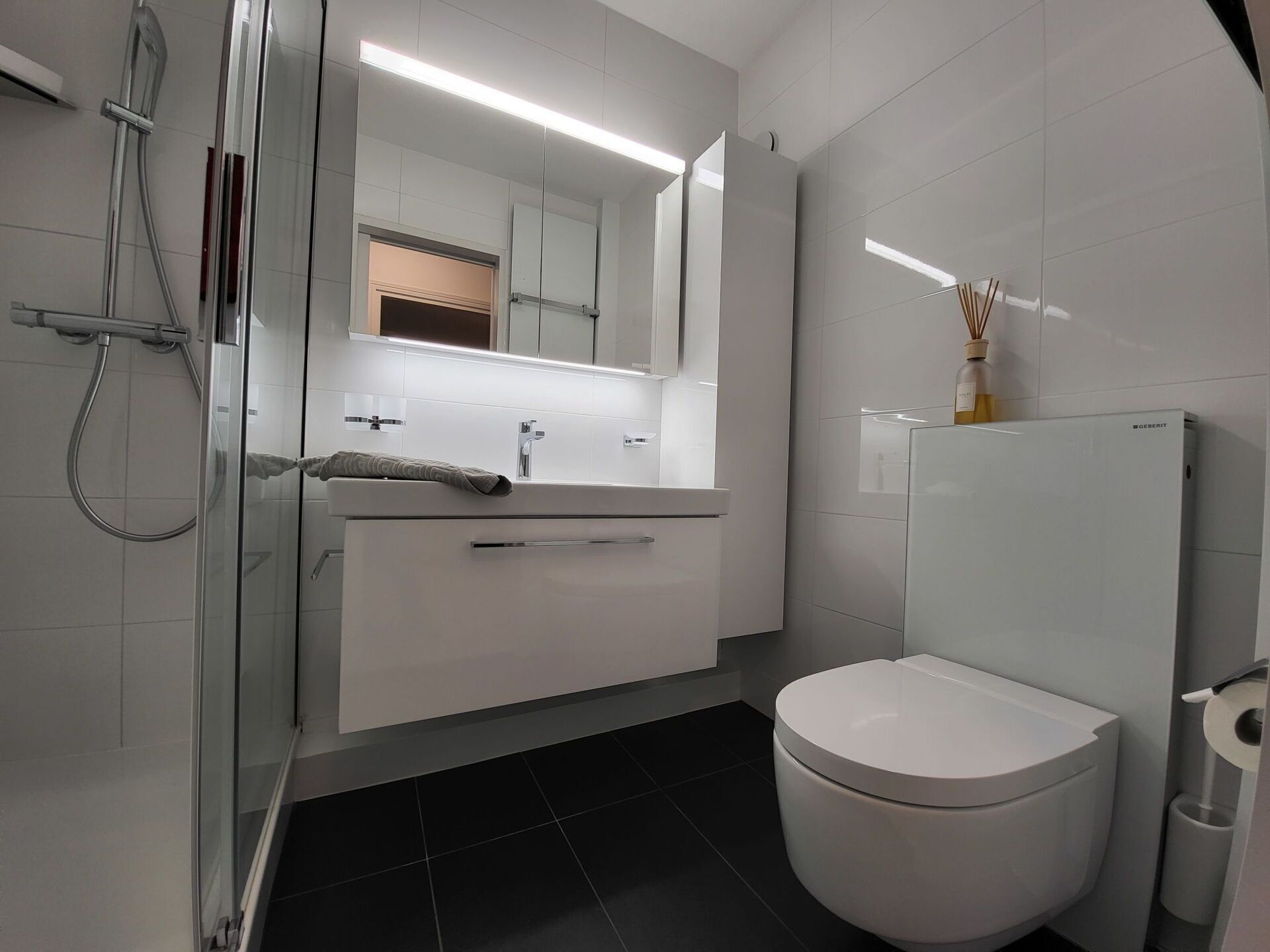 A modern bathroom with a glass shower enclosure, a white sink with a towel, and a toilet.