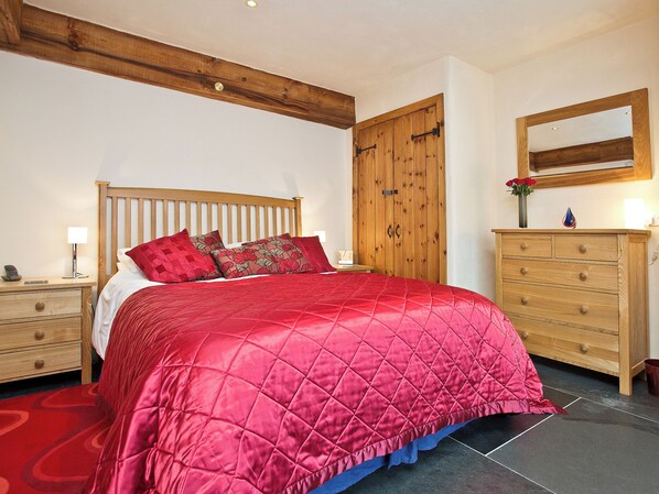 A bedroom with a wooden bed frame, a red bedspread, a wooden dresser, and a mirror above the dresser. - 3 bedroom accommodation in St Issey, Wadebridge (St Issey, Wadebridge)
