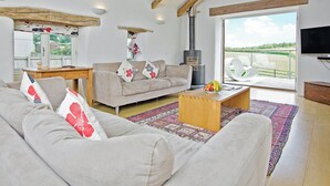 Een woonkamer met een bank, salontafel en een televisie. Er is een open haard en een raam met uitzicht.