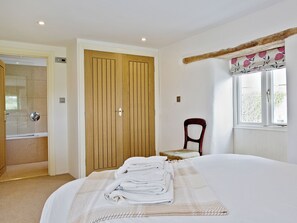 Habitación de hotel con cama, armario de madera, una silla, ventana con cortinas y baño con ducha.