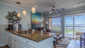 A kitchen with granite countertops, a large island, white cabinetry, and a dining area with a view.