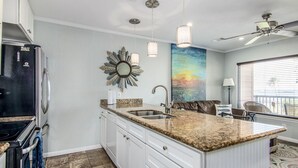 A kitchen with granite countertops, a sink, a refrigerator, and a ceiling fan.