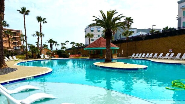 A swimming pool with lounge chairs, palm trees, and a small gazebo.