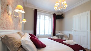 Een goed verlichte hotelkamer met een groot bed, een zithoek met een tafel en stoelen, een televisie en een deur.