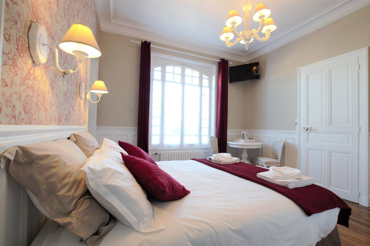 Une chambre d’hôtel bien éclairée, dotée d’un grand lit, d’un coin salon avec une table et des chaises, d’une télévision et d’une porte.