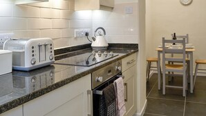 A modern kitchen with white cabinetry, a granite countertop, a toaster, a kettle, and a dining area with a table and chairs. - 2 bedroom accommodation in Keswick (Keswick)