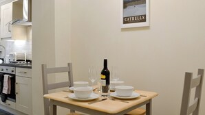 A dining area with a table set for two, a wine bottle, and a framed picture of a mountain landscape. - 2 bedroom accommodation in Keswick (Keswick)
