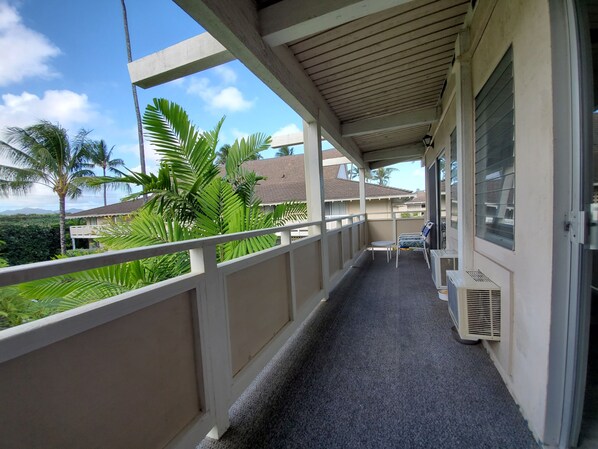 A balcony with a view of palm trees and houses, a small table, and a chair. - Central location, Steps to the Beach, & Convenience Shops, restaurants. (Kapaa)