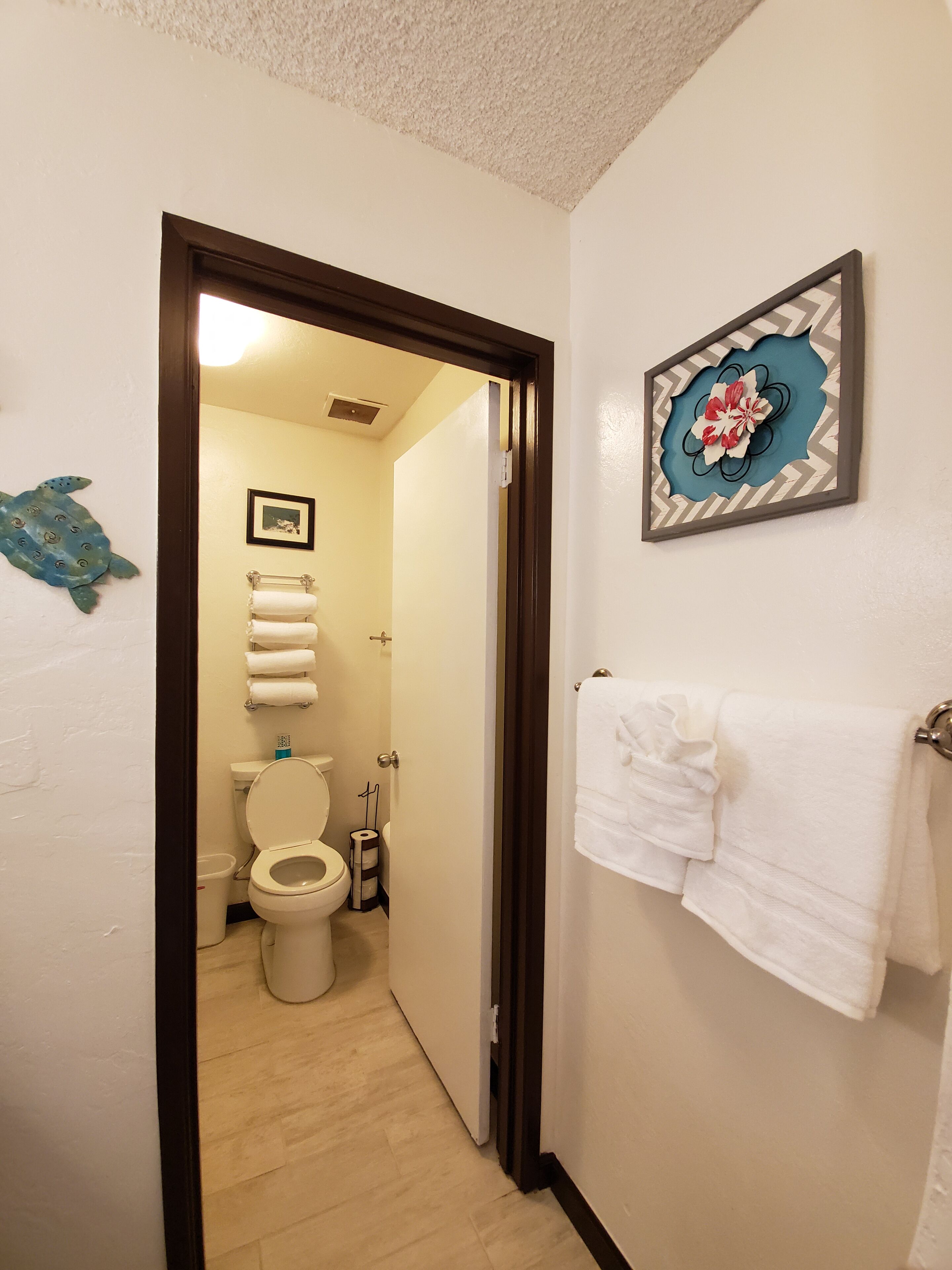 Un baño con inodoro, toallero con toallas blancas y un adorno en la pared.