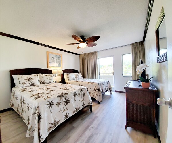 A hotel room with two beds, a ceiling fan, a desk with a potted plant, and a window with curtains.
