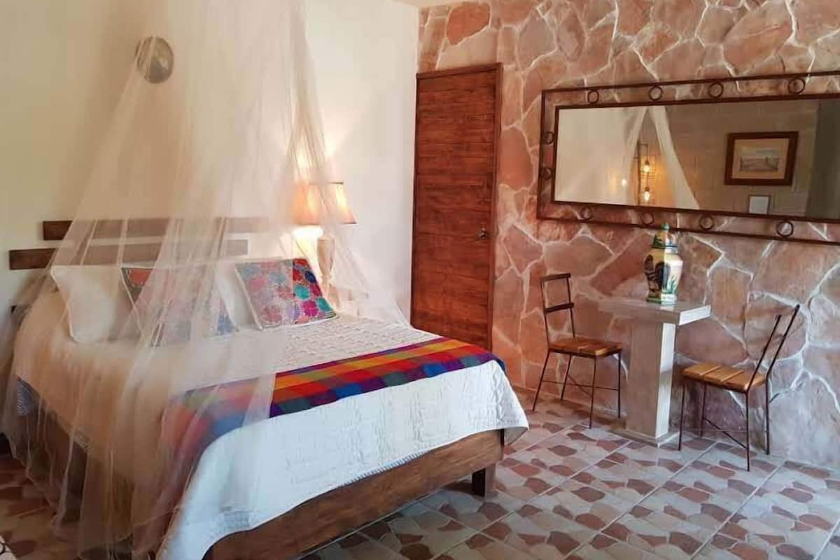 Um quarto com cama, escrivaninha, cadeira e parede de pedra.