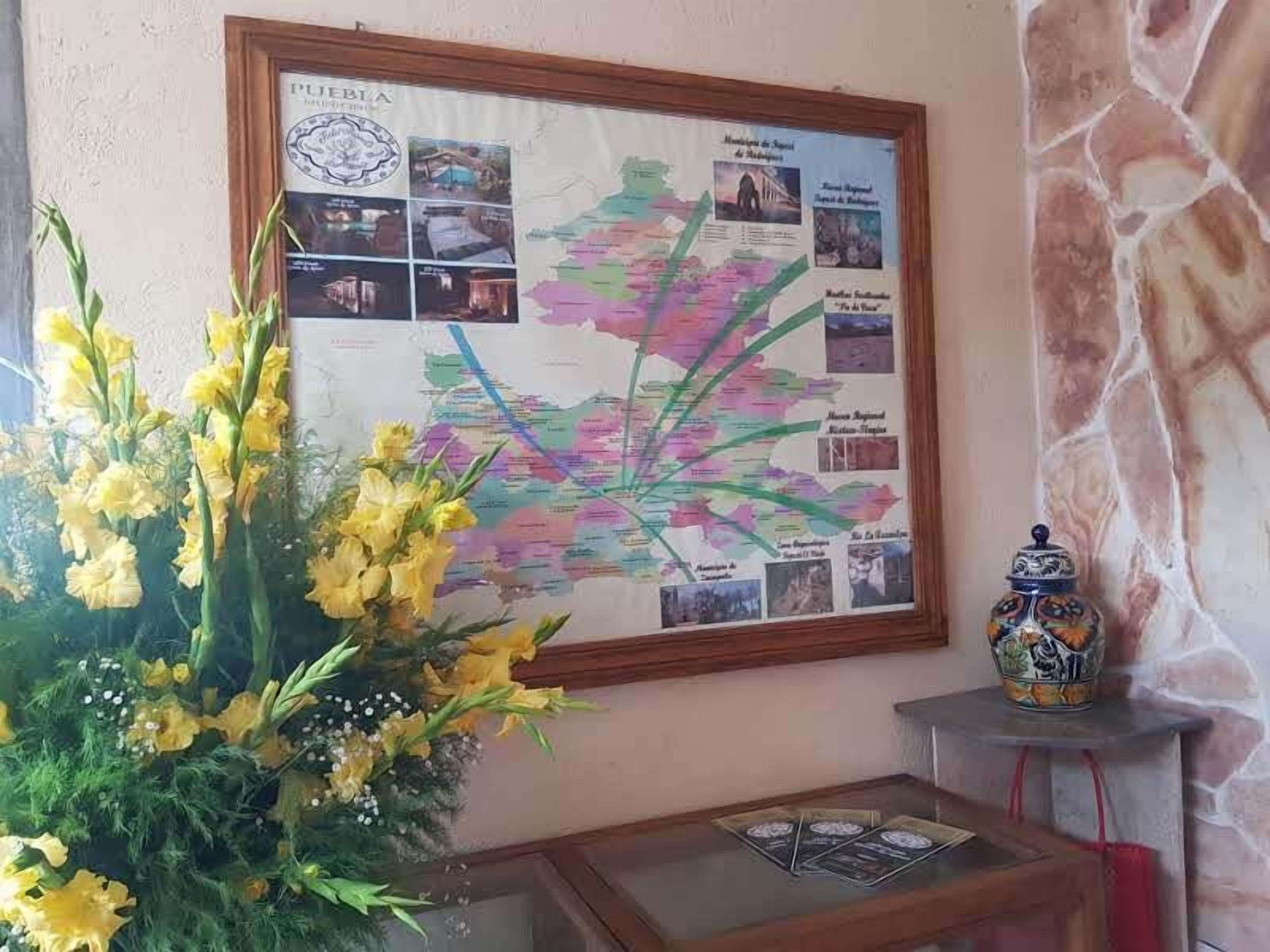 A framed map with regional photos, a vase of yellow flowers, and a decorative ceramic pot on a table.