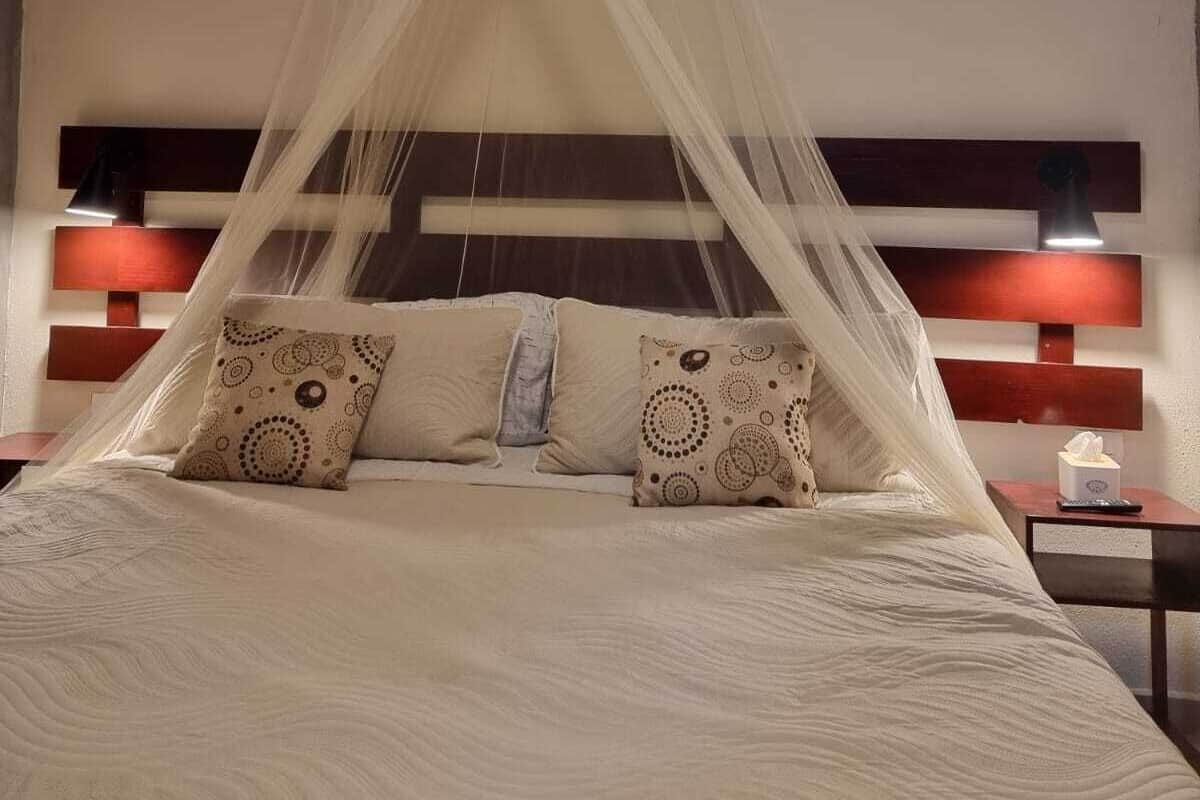 Uma cama com dossel, duas mesas de cabeceira com luminárias e uma mesa de cabeceira com caixa de lenços.