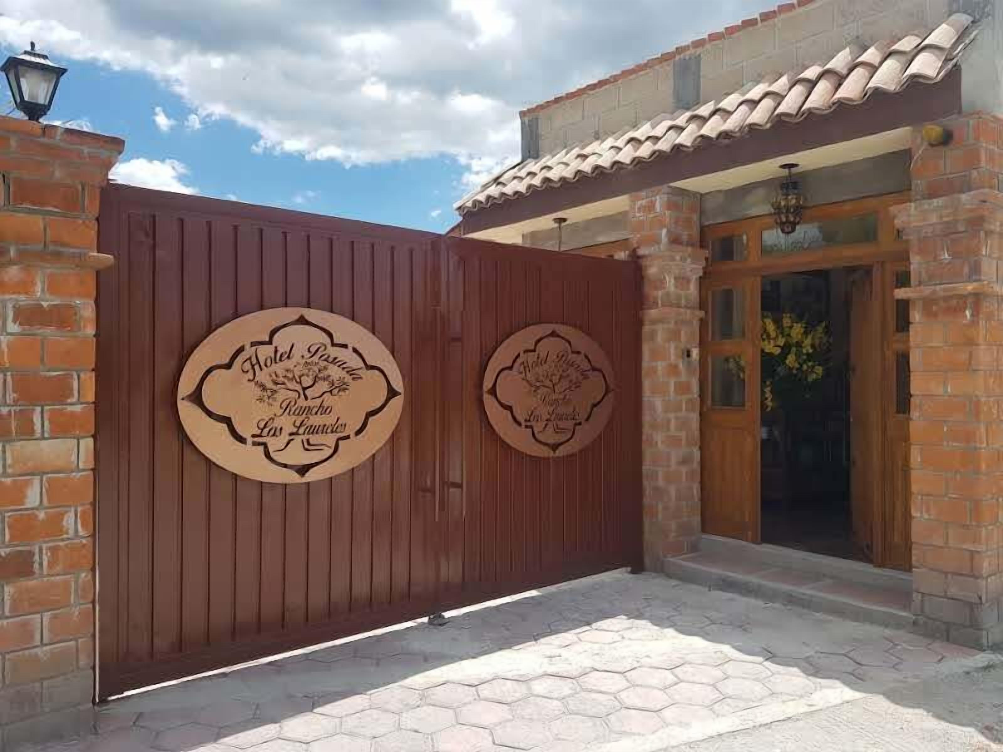 Una entrada con reja y dos letreros de madera que indican 'Hotel Posada Rancho Los Laureles'.
