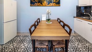 Un comedor con mesa de madera, sillas, un florero con flores, un refrigerador y una zona de cocina con gabinetes y un lavamanos.