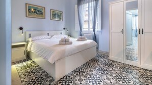 Un dormitorio con cama, mesitas de noche, armario y ventana con cortinas.